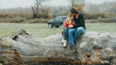 A couple embraces tenderly on a large fallen tree, set against a serene natural landscape.